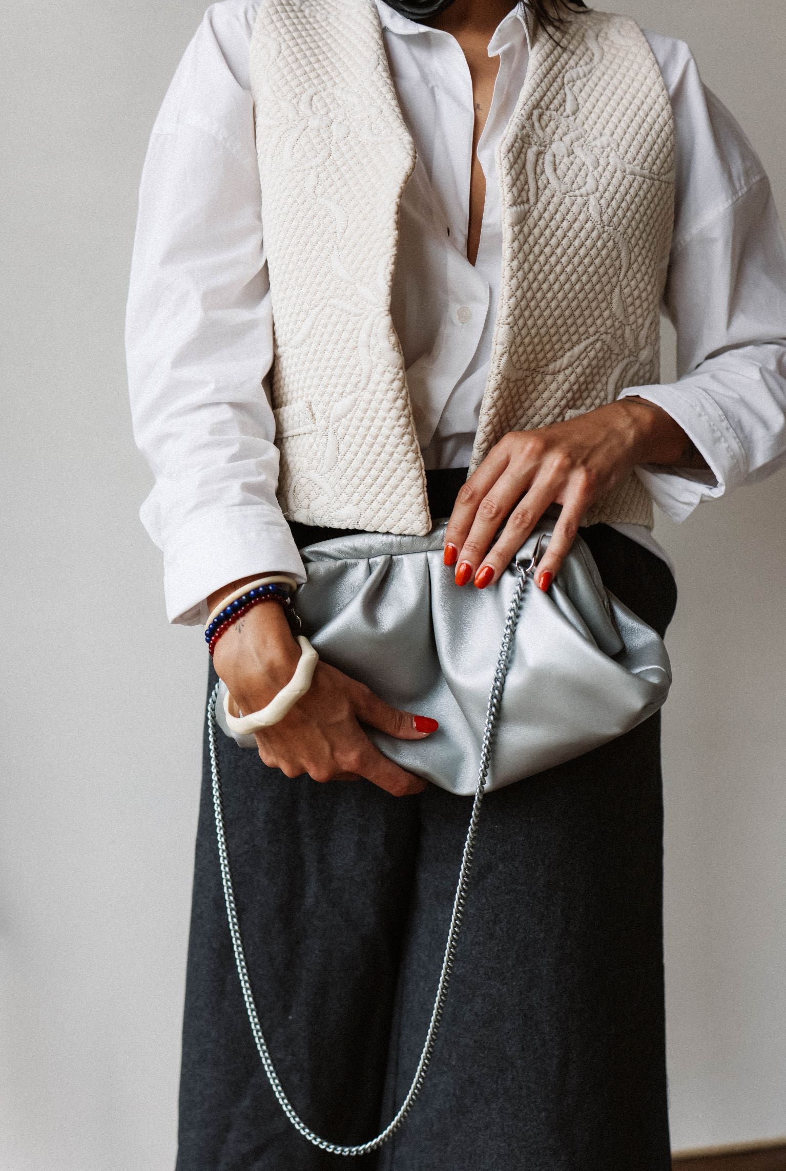 fille qui tient à la main un sac argent by ninette et porte une veste sans manche blanche upcyclée